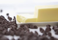 Vue rapprochée des pépites de chocolat et du beurre coupé sur plaque — Photo de stock