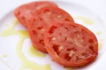 Tomates en rodajas en una placa blanca rociados con aceite de oliva en plato blanco - foto de stock