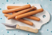 Top view of Frankfurters sausages with knife on chopping board — Stock Photo