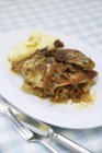 Roast pheasant on a bed of wine sauerkraut with mashed potato in white plate over cloth with fork and knife — Stock Photo