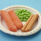 Fish fingers with peas on white plate over blue surface — Stock Photo