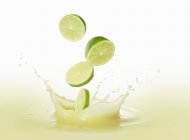 Limes falling into lime juice — Stock Photo