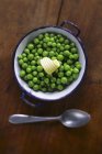 Cooked peas with a curl of butter in saucepan over wooden surface with spoon — Stock Photo