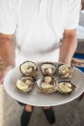 Closeup cropped view of man holding raw scallops with lemon on plate — Stock Photo