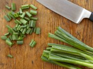 Scallions sliced on wooden surface with knife — Stock Photo