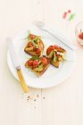 Crostini con pomodori e rucola su piatto bianco con forchetta e coltello — Foto stock