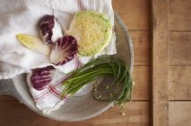 Assorted greens including, radicchio, lettuce, chives, endive on plate over wooden surface — Stock Photo
