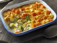 Haddock gratin with sweet potatoes and broccoli on white dish over wooden surface — Stock Photo