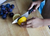Дитина розрізає лимон навпіл з ножем — стокове фото