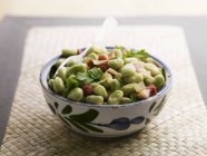Broad bean and ham in bowl over straw mat — Stock Photo