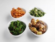 Accompagnements de légumes cuits à la vapeur et pommes de terre rôties dans des bols à la surface blanche — Photo de stock