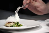 Chef plating up fish and broad bean dish during service at working restaurant — Stock Photo