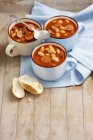 Beans with sausage and bacon in tomato sauce in pots over wooden surface with towel — Stock Photo