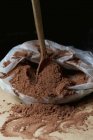 Closeup view of a wooden spoon in a plastic bag of cocoa powder — Stock Photo