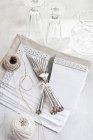 Elevated view of tied forks and knives with strings, towels and glasses on a white surface — Stock Photo