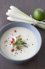 Coconut soup with chicken strips, bamboo shoots, coriander and black sesame seed with a bundle of lemongrass and a lime next to it — Stock Photo