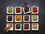 Top view of various spices in square dishes on a chalkboard surface — Stock Photo