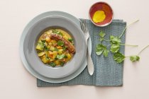 Close up of Green kale and potato curry with lamb sausages on grey plate over towel — Stock Photo