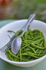 Зеленая фасоль на белой тарелке с вилкой и ложкой — стоковое фото