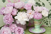 Pink and white peonies in a retro vase in front of a wall painted with a stencil pattern — Stock Photo