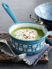 Spicy pea soup in saucepan over textile on wooden desk — Stock Photo
