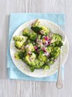 Steamed broccoli with red onion vinegar  on white plate with fork over towel — Stock Photo