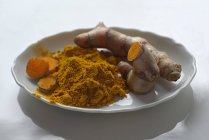 Turmeric powder and roots on plate — Stock Photo