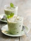 Iced courgette soup with mint in glasses over plates on wooden surface — Stock Photo