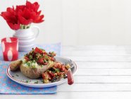 A baked potato filled with ratatouille on white plate with fork over towel — Stock Photo