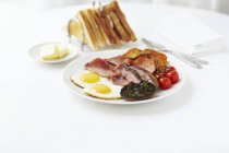 Café da manhã de ovos fritos, bacon, salsichas, cogumelos fritos, batatas fritas e tomates servidos com uma torrada — Fotografia de Stock
