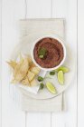 Tomato hummus with tortilla chips and lime wedges  on white plate over towel on white surface — Stock Photo