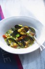 Mussel stew with vegetables on white plate with spoon — Stock Photo