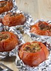 Stuffed, grilled tomatoes in aluminium foil over wooden surface — Stock Photo