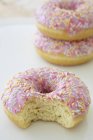 Nahaufnahme ganzer und gebissener rosa glasierter Donuts mit Zuckerstreusel — Stockfoto
