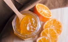 A jar of marmalade and fresh, halved oranges over wooden surface — Stock Photo