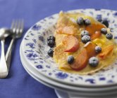 Sweet omelette with blueberries, peaches and icing sugar on white and blue plate — Stock Photo