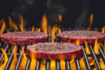 Raw hamburgers on flaming barbecue — Stock Photo