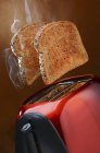 Closeup view of smoking wholemeal toast jumping out of a red toaster — Stock Photo