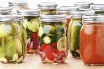 Jars of Mediterranean preserved vegetables: cucumber, courgettes, pepper, onion, lemon and tomato sauce — Stock Photo