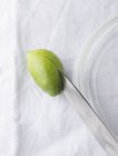 Une olive verte coupée en deux avec un couteau sur la surface textile — Photo de stock