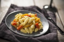 Nhoque com pimentas e tomates em prato preto sobre toalha — Fotografia de Stock