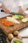 Шеф-повар режет овощи с ножом в руках над доской — стоковое фото