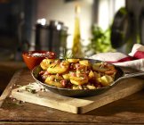 Fried potatoes with bacon and rosemary in a rustic pan over wooden desk — Stock Photo
