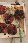 Poivrons rouges rôtis sur plaque de cuisson blanche sur une surface en bois — Photo de stock