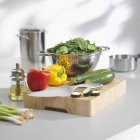 Espinafre em um escorredor e verduras em uma tábua de corte — Fotografia de Stock