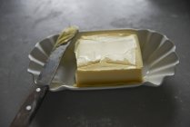 Vista close-up de manteiga em um prato de cerâmica com uma faca velha — Fotografia de Stock