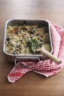 Chard gratin in baking dish with spoon on wooden surface with towel — Stock Photo