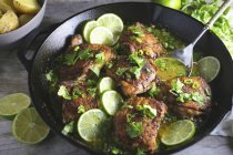 Vue rapprochée des cuisses de poulet avec des tranches de citron vert et des herbes dans la casserole — Photo de stock