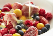 Вид крупным планом на ванильный соус, выливаемый на различные ягоды — стоковое фото