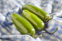 Three fresh, raw green jalapeos over cloth — Stock Photo